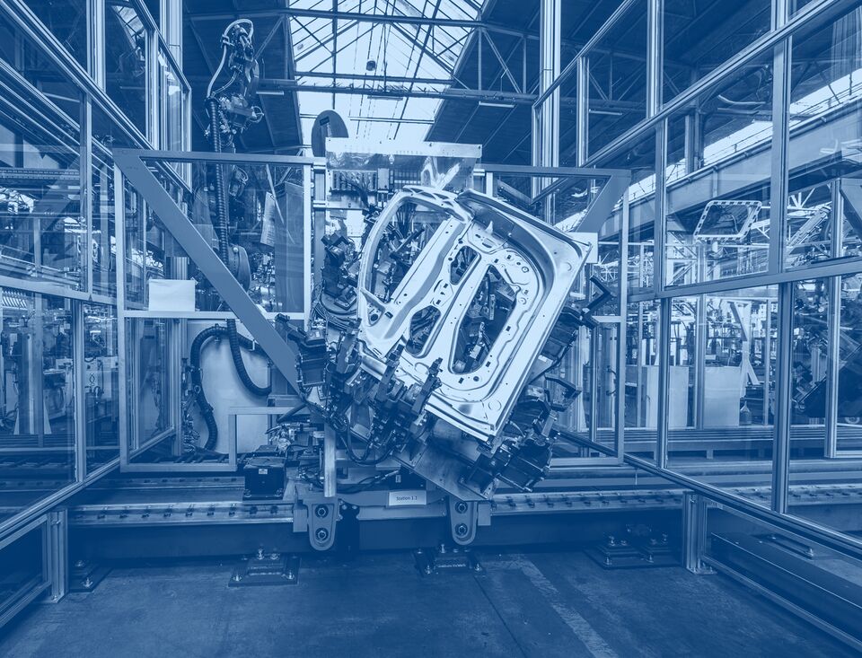 Mittlere Aufnahme einer Autotür, die in einer Bearbeitungsanlage eingespannt ist, umgeben von technischen Vorrichtungen.